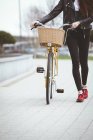 Low section of woman with bicycle walking on pavement — Stock Photo
