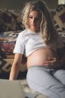 Mulher grávida tocando sua barriga na sala de estar em casa — Fotografia de Stock