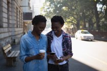 Jumeaux frères et sœurs utilisant le téléphone mobile tout en marchant sur le trottoir dans la rue de la ville — Photo de stock