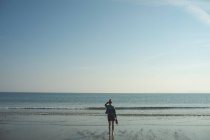 Вид ззаду жінки, що стоїть на морському пляжі в сонячний день — стокове фото
