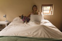 Ragazza con il suo cane utilizzando il computer portatile in camera da letto a casa — Foto stock