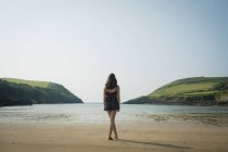 Вид ззаду жінки, що стоїть на пляжі зі схрещеними ногами — стокове фото