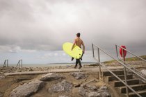 Surfista con tabla de surf caminando hacia el mar en un día soleado - foto de stock