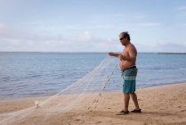 Pescatore che tiene una rete da pesca su una spiaggia — Foto stock
