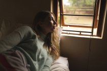 Девушка смотрит в окно в спальне дома — стоковое фото