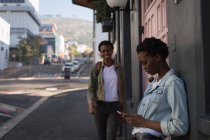 Fratelli gemelli utilizzando il telefono cellulare in strada in una giornata di sole — Foto stock