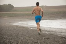 Rear view of man jogging on shore at beach — Stock Photo