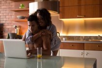 Couple utilisant un ordinateur portable dans la cuisine à la maison — Photo de stock
