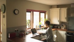 Femme utilisant un ordinateur portable dans la cuisine à la maison — Photo de stock