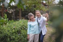 Fisioterapeuta e mulher idosa tomando uma selfie no jardim — Fotografia de Stock