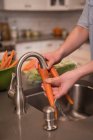 Partie médiane de la femme laver la carotte dans la cuisine à la maison — Photo de stock