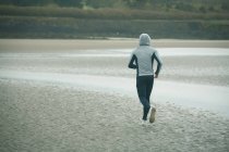 Visão traseira do homem com capuz correndo na praia — Fotografia de Stock