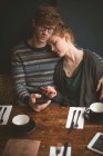 Casal jovem abraçando e usando telefones celulares no café — Fotografia de Stock