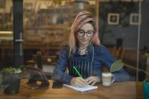Молодая женщина делает заметки в кафе — стоковое фото