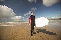 Surfer mit Surfbrett steht an einem sonnigen Tag am Strand — Stockfoto