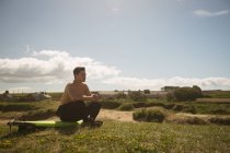 Surfeur assis sur la planche de surf sur la plage par une journée ensoleillée — Photo de stock