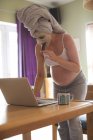Mujer embarazada con crema facial usando portátil en casa - foto de stock