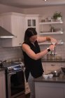 Mulher despejando caneca em jarro na cozinha em casa — Fotografia de Stock