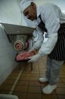 Carnicero usando máquina para picar carne en carnicería - foto de stock