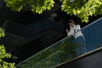 Mann benutzt Handy und trinkt an einem sonnigen Tag Kaffee auf Bürobalkon — Stockfoto