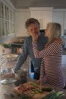 Seniorin füttert Mann, während sie zu Hause in der Küche Essen zubereitet — Stockfoto
