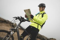 Young man with cycle reading map at the beach — Stock Photo