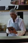 Carnicero atento usando tableta digital en carnicería - foto de stock