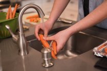 Partie médiane de la femme laver la carotte dans la cuisine à la maison — Photo de stock