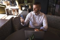 Empresário usando telefone enquanto trabalhava em laptop no refeitório no escritório — Fotografia de Stock