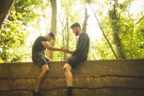 Un homme apte à aider son coéquipier à escalader un mur en bois au camp d'entraînement — Photo de stock