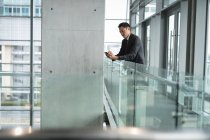 Geschäftsmann mit Handy an Geländer im Büro gelehnt — Stockfoto