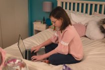 Chica usando el ordenador portátil en el dormitorio en casa - foto de stock