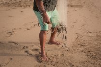 Partie basse du pêcheur tenant un filet de pêche sur la plage — Photo de stock