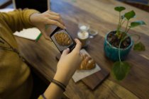 Junge Frau fotografiert Croissant, das auf dem Tisch im Café serviert wird — Stockfoto