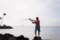 Vista trasera de un pescador pescando en una playa - foto de stock