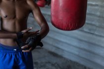 Partie médiane du boxeur masculin attachant enveloppement à la main sur la main à la salle de fitness — Photo de stock