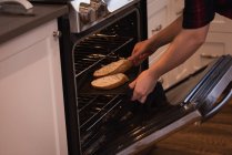 Mujer poniendo rebanada de pan dentro del owen en la cocina en casa - foto de stock