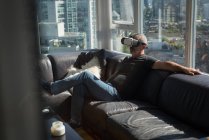 Hombre usando auriculares de realidad virtual en la sala de estar en casa - foto de stock