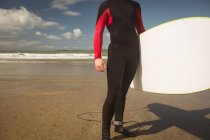 Серфер с доской для серфинга, стоящий на пляже в солнечный день — стоковое фото