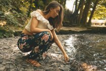 Close-up of woman crouching near the river coast in green forest — Stock Photo