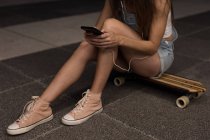 Female skater sitting on skateboard and using mobile phone in the street — Stock Photo