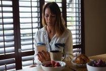 Жінка, використовуючи мобільний телефон кухні в домашніх умовах — стокове фото