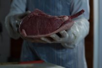 Средняя часть мясника держит мясо в руках в мясной лавке — стоковое фото