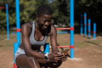 Athlète féminine souriante utilisant son téléphone près des bars — Photo de stock