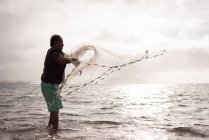 Pescatore gettando rete da pesca sulla spiaggia al crepuscolo — Foto stock