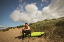 Серфер сидить на дошці на пляжі в сонячний день — стокове фото