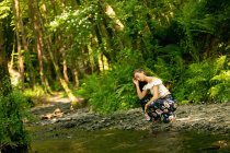 Beautiful woman crouching near the river coast in green forest — Stock Photo