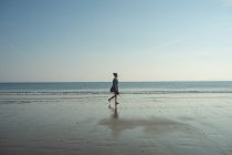 Femme marchant sur la plage par une journée ensoleillée — Photo de stock