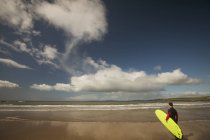 Surfista com prancha olhando para o mar da praia em um dia ensolarado — Fotografia de Stock