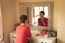 Женщина наносит макияж перед зеркалом в спальне дома — стоковое фото